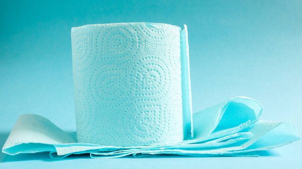 Blauwe rol modern toiletpapier op een blauwe achtergrond. Een papierproduct op een kartonnen hoes, gebruikt voor sanitaire doeleinden van cellulose met uitsparingen voor gemakkelijk scheuren. Tekening in reliëf. - Foto, afbeelding