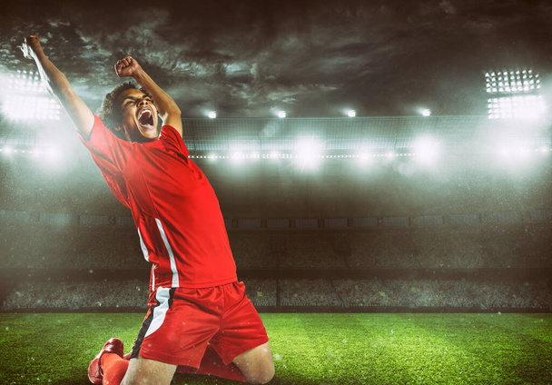 Soccer striker in red uniform rejoices for the victory at the stadium - Фото, изображение