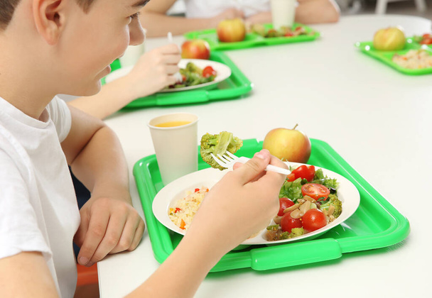 Menino da escola comendo comida deliciosa à mesa
 - Foto, Imagem