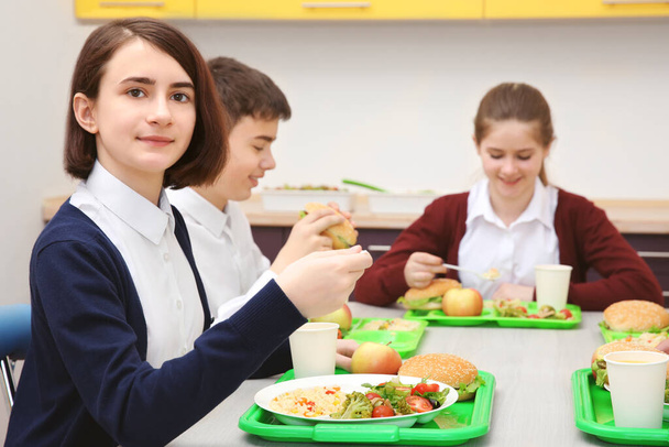 Children sitting at table in school cafeteria while eating lunch - Photo, Image