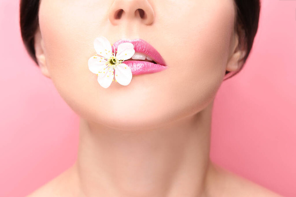 色の背景に唇の間に花を持つ美しい若い女性 - 写真・画像