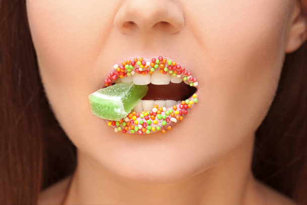Belle jeune femme avec maquillage créatif tenant la marmelade dans la bouche, gros plan
 - Photo, image