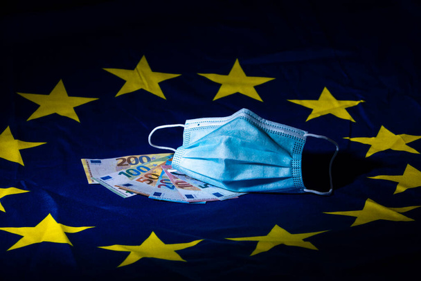 ráncos arcmaszk és pénz egy európai zászlón, amely az egészségügyi üzlet fogalmát illusztrálja - Fotó, kép