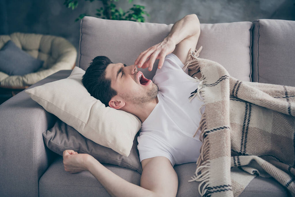 Portrait of his he nice attractive tired sleepy guy lying on divan waking up resting yawning healthy regime at modern industrial loft brick interior style living-room indoors - Foto, immagini