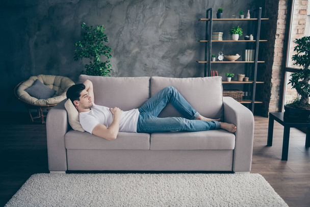 Profile side view portrait of his he nice attractive guy lying on divan resting free time pause break at modern industrial loft brick interior style living-room - Foto, Imagen