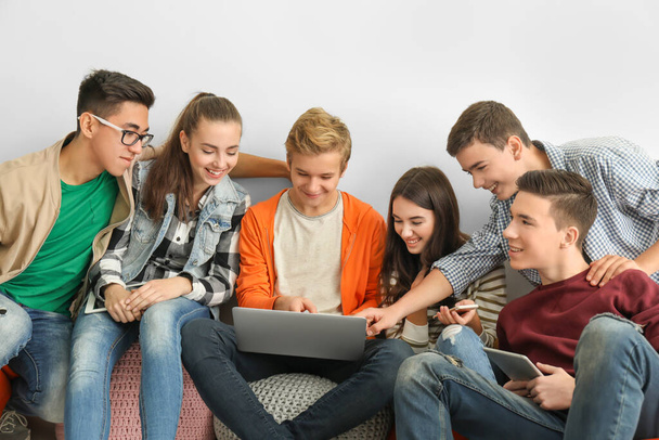 Группа подростков с современными устройствами, сидящих возле белой стены
 - Фото, изображение