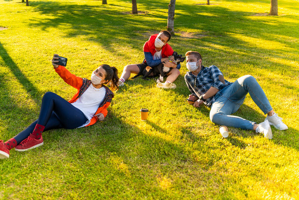 Wesoły student robi selfie z przyjaciółmi siedzącymi na trawie - Zdjęcie, obraz