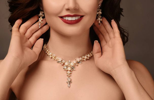 Mooie vrouw met elegante sieraden op grijze achtergrond, close-up - Foto, afbeelding