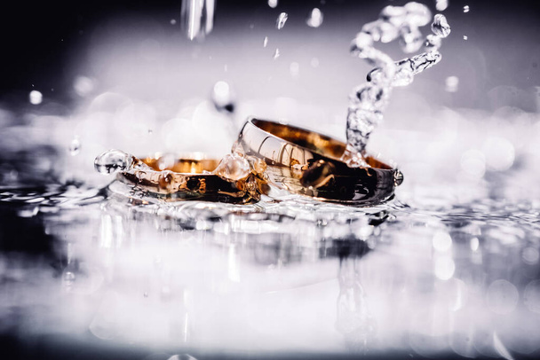 Two wedding rings in water splashes laying on flat surface - Photo, Image