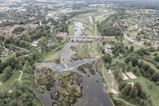 Schöne Panorama-Luftaufnahme von der fliegenden Drohne zum Venta Rapid Wasserfall, dem breitesten Wasserfall Europas und der drittlängsten Ziegelbrücke Europas an einem Sommertag in Kuldiga, Lettland. (Reihe) - Foto, Bild