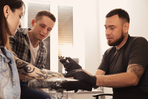Professional tattoo master teaching young specialist in salon. Internship concept - Photo, Image