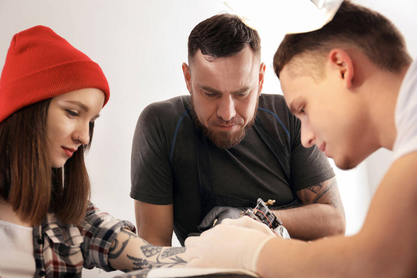 Professional tattoo master teaching young specialist in salon. Internship concept - Photo, Image