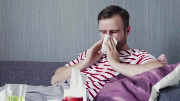 Ein Mann hustet heftig und pustet sich die Nase, während er auf einer Couch im Wohnzimmer sitzt - Filmmaterial, Video