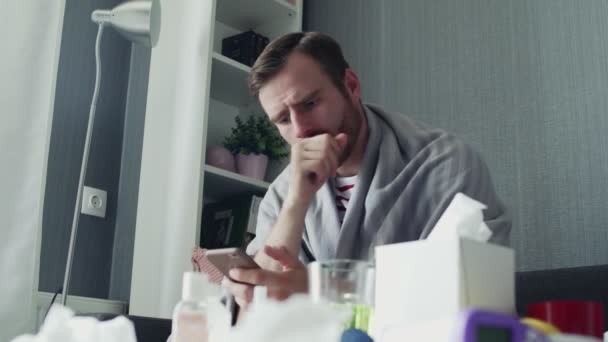 Молодой человек, сидящий на диване использовать телефон кашель в доме пить чай грустный несчастный грипп больной взрослый холодная болезнь человека болезнь аллергия на вирус замедленной съемки портрет крупным планом
 - Кадры, видео