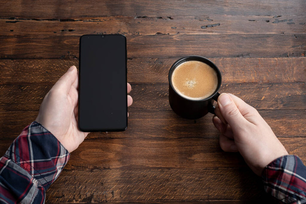 Gros plan d'un homme utilisant un téléphone intelligent mobile, envoyant des massages à la maison avec du café. Téléphone avec écran noir, SMS, appels vidéo. Travail à domicile.  - Photo, image