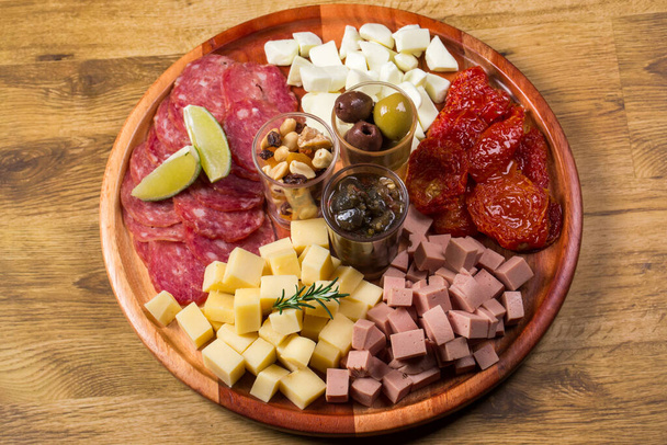 round board with various antipasti appetizers. Cheese, salami, olives, nut mix and sun-dried tomatoes. top view. - Фото, зображення