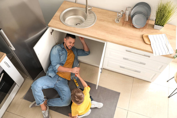 Pequeño hijo ayudando a su padre a reparar fregadero en la cocina
 - Foto, imagen