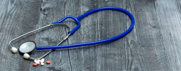 A blue medical stethoscope and a variety of medical pills sit on a wooden surface. - Photo, Image