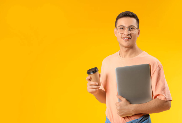 Portrait of young man with laptop and coffee on color background - 写真・画像