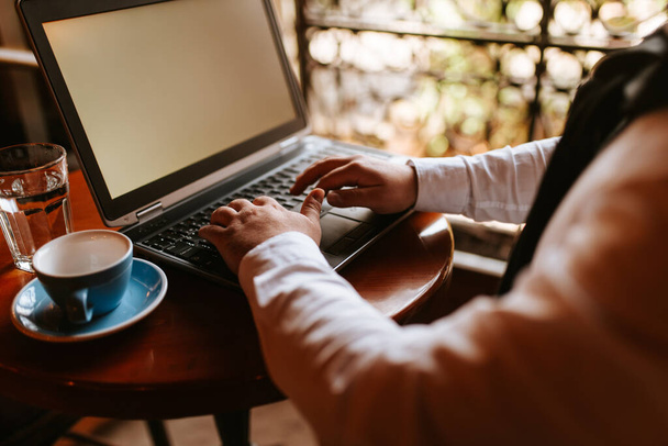 Der junge Geschäftsmann sitzt in einem Café und arbeitet am Computer. Ein Computer und eine Tasse Kaffee - Foto, Bild