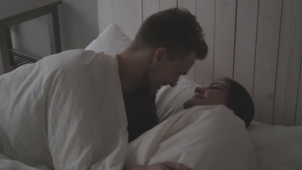 Young couple, man and woman at home in the bedroom. They roll on the bed, make fun, fight pillows and hug. Family evening. - Materiał filmowy, wideo
