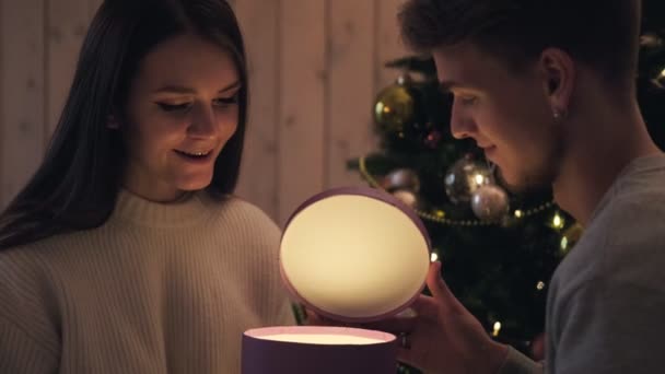 A young couple, a man and a woman at home open a gift box. They are surprised and rejoiced. - Imágenes, Vídeo