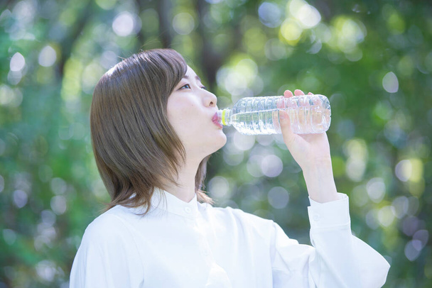 Asiatische junge Frau trinkt Wasser in einer transparenten Plastikflasche im Freien - Foto, Bild