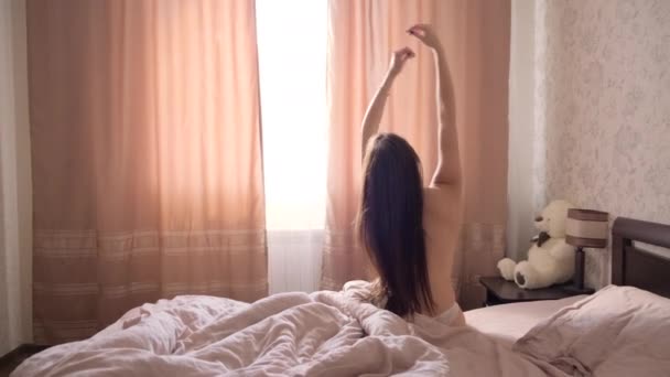 Young topless girl with long dark hair wakes up in a large bed in the bedroom - Πλάνα, βίντεο