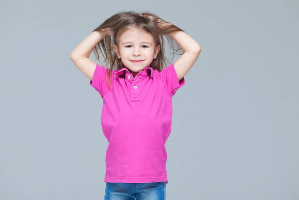 portrait of funny active little girl wearing casual clothes: jeans and pink t-shirt isolated on grey studio background - Foto, Imagen