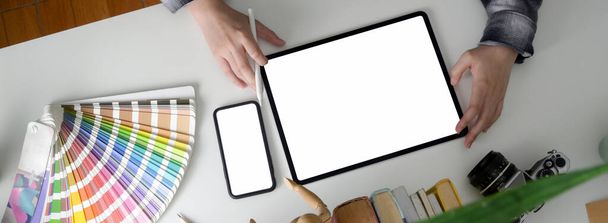 Nad głową ujęcie projektantki pracującej z pustym ekranem tabletu, smartfona i materiałów projektanta na białym biurku  - Zdjęcie, obraz