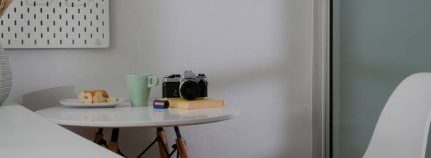 Schnappschuss von Couchtisch mit Kaffeebecher, Kamera, Brot und Kopierraum auf weißem Kreis-Schreibtisch  - Foto, Bild