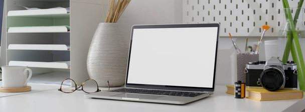 Обрезанный снимок минимального рабочего стола с чистым экраном ноутбука, канцелярских принадлежностей и украшений на белом столе
  - Фото, изображение