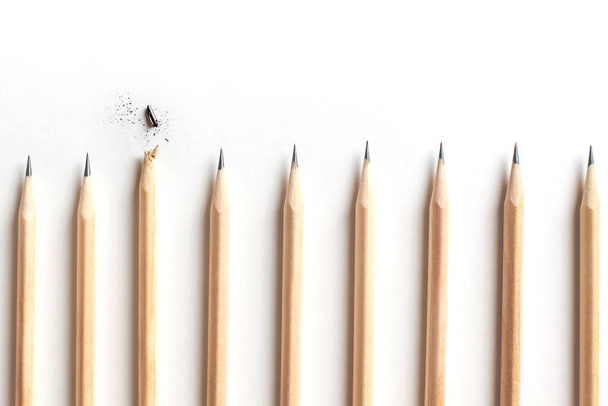 Side view of row of even beautiful sharpened pencils lying on white table with one lying above and broken. Concept of tired leader and an eccentric employee who burned out early. Advertising space - Foto, afbeelding