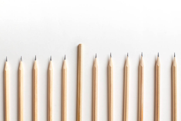 Beautiful neatly sharpened pencils made of wood lie in rare row next to an unsharpened pencil on white background. Concept of new employee who does not know the rules of new team. Advertising space - Foto, afbeelding