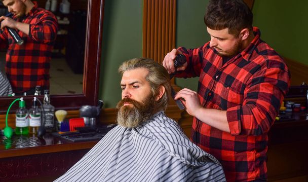 Guy with long dyed blond hair close up. Do not cut your own hair. Hipster client getting haircut. Barber with scissors and client. Barber works on hairstyle for bearded man barbershop background - Foto, Imagen