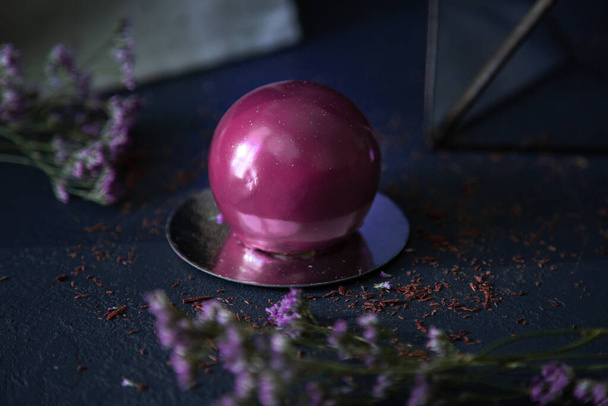 Deliciosa sobremesa de bola de chocolate elegante no fundo escuro com flores cor violeta
 - Foto, Imagem
