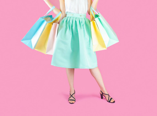 The woman low body part wore blue skirt and black high heels. Carrying a shopping bag in many pastel colors on pink background selective focus - Photo, image