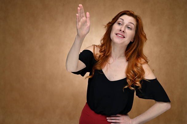 Studio photo portrait of a caucasian young woman in a black blouse with long red hair on a beige background. The model shows different emotions with a smile. - Foto, Imagem