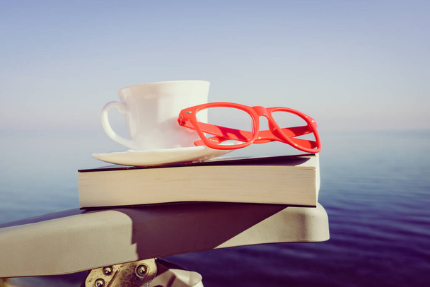 Reading on holidays. Coffee cup and book on chair outdoors against blue sea water background. - Foto, Bild