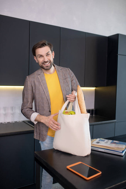Young bearded man holding a bag with food and looking cheerful - Φωτογραφία, εικόνα