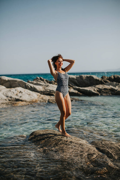 Pretty young woman in bikini walking on rocks by the sea - 写真・画像
