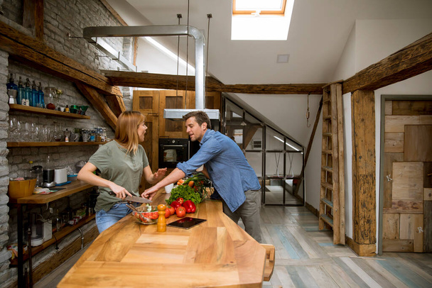 Loving young couple cutting vegetables together in the rustic kitchen - Foto, Imagem