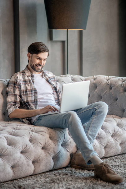Dark-haired bearded man on the couch with a laptop. - Photo, Image