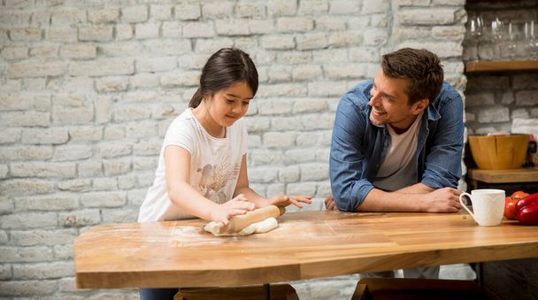 Fiatal apa és aranyos lánya tésztát keresnek rusztikus otthoni konyhában. - Fotó, kép
