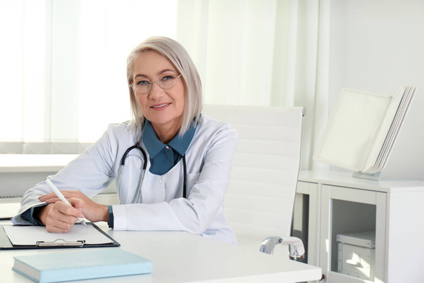 Portrait of mature female doctor in white coat at workplace - Fotoğraf, Görsel