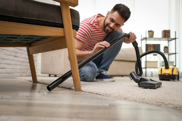 Young man using vacuum cleaner at home - Foto, imagen