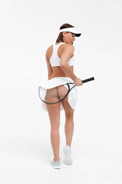 Back view of sexy lady in erotic sportswear with tennis racket lifting up skirt and showing buttocks - Photo, image