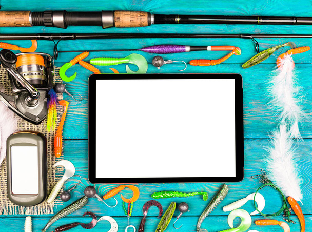 Fishing rod, tackles and fishing baits, reel on wooden board background with tablet computer isolated white screen. Empty space for text - Photo, Image