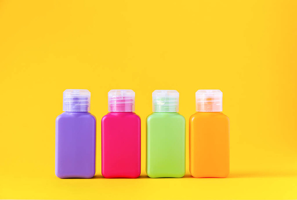 Πολύχρωμα πλαστικά μπουκάλια για προϊόντα περιποίησης του δέρματος σε έντονο κίτρινο φόντο - Φωτογραφία, εικόνα