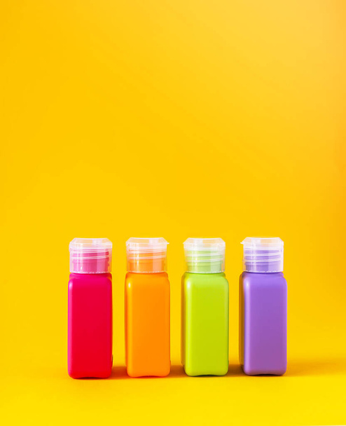 Красочные пластиковые бутылки для изделий из кожи на ярко-желтом фоне
 - Фото, изображение